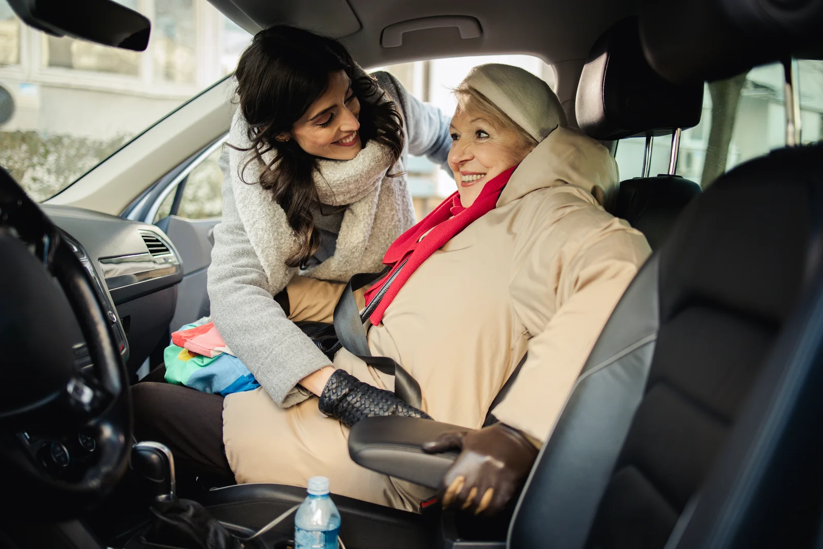 Eine Begleiterin hilft einer älteren Frau beim Anschnallen im Auto.