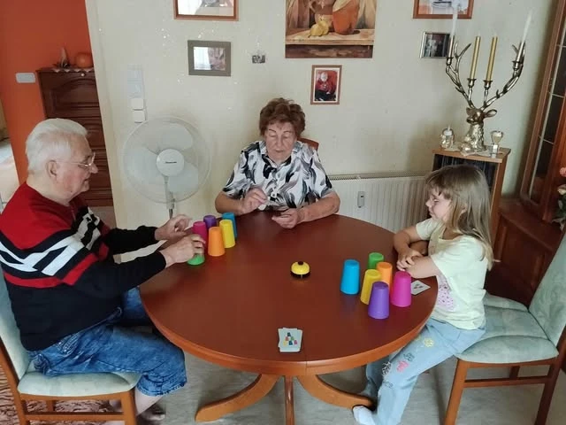 Zwei ältere Menschen und ein Kind spielen am Tisch mit bunten Bechern.