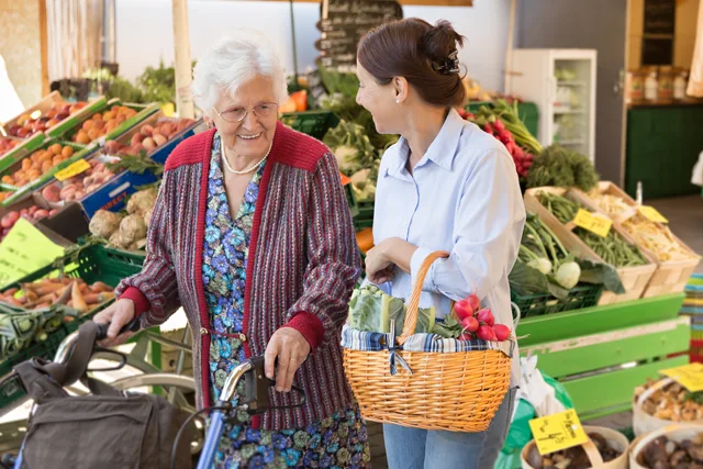 Eine ältere Frau und ihre Begleiterin kaufen an einem Obst- und Gemüsestand ein.