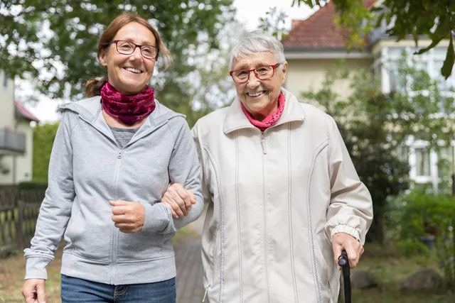 Zwei ältere Menschen gehen gemeinsam Arm in Arm auf einem Weg im Grünen.