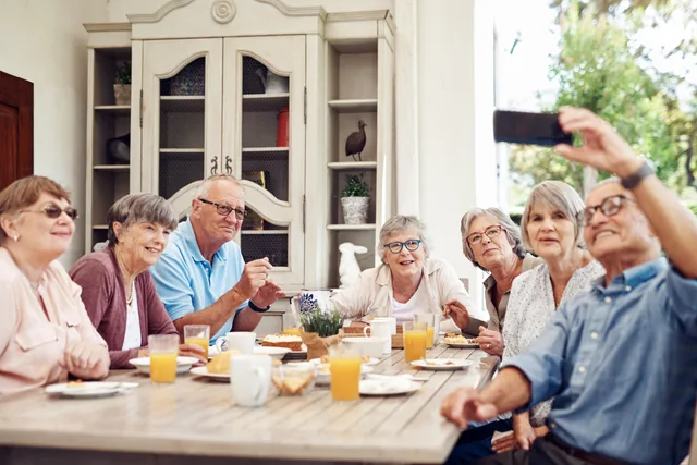 Eine Gruppe älterer Menschen sitzt am Tisch und macht gemeinsam ein Foto mit dem Smartphone.