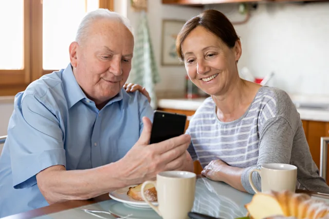Ein älterer Mann und eine Frau schauen gemeinsam auf ein Smartphone.