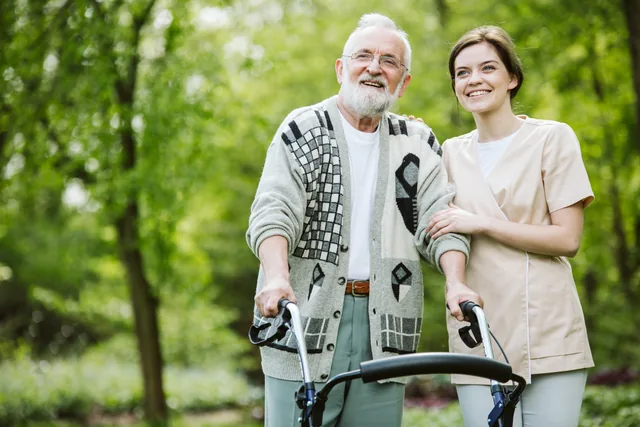 Ein älterer Mann steht mit einem Rollator neben einer Begleiterin im Grünen.